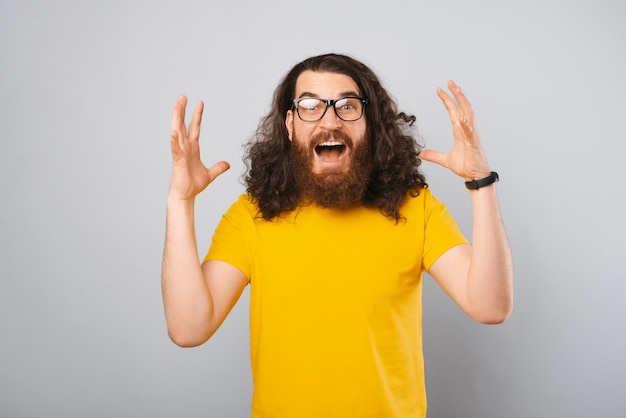 Zaskoczony brodaty mężczyzna w żółtej koszulce robi gest wow na szarym tle Strzał studio