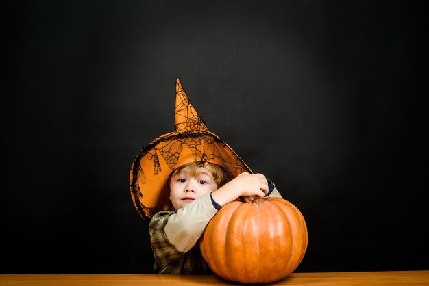 Zaskoczony chłopiec w kapeluszu wiedźmy z dynią halloween. Dziecko z dynią. Wesołego Halloween. Święta Halloween. Cukierek albo psikus. Latarnia z dyni. Przygotowanie do Halloween. Chłopiec przebrany za cukierka albo psikusa.