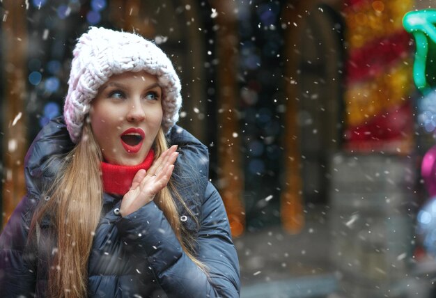 Zaskoczony ładna kobieta spacerująca na targach noworocznych podczas opadów śniegu. Pusta przestrzeń