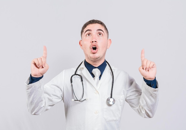 Zaskoczony lekarz wskazujący awans w górę Mężczyzna lekarz patrzący i wskazujący w górę na białym tle Zaskoczony lekarz wskazujący reklamę w górę