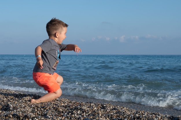 Zaskoczony mały chłopiec uciekający przed falami, mały chłopiec sam na plaży.