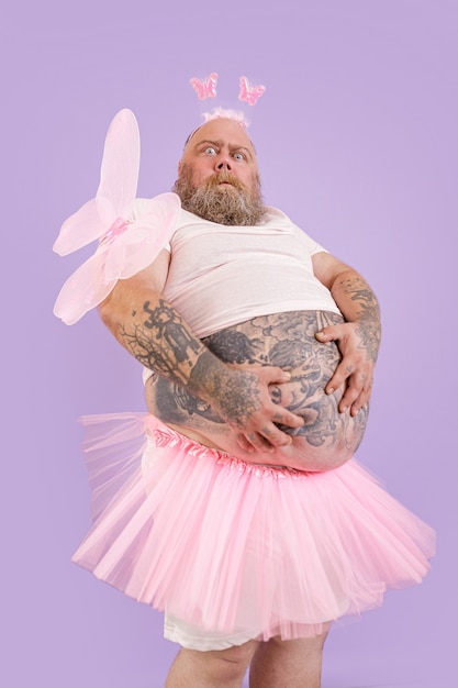 Zaskoczony pulchny mężczyzna w stroju wróżki trzyma duży brzuch na fioletowym tle