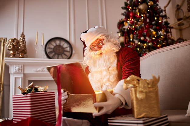 Zaskoczony Święty Mikołaj magicznym świecącym prezentem w pobliżu pięknej choinki. Nowy rok i Wesołych Świąt, koncepcja Wesołych Świąt