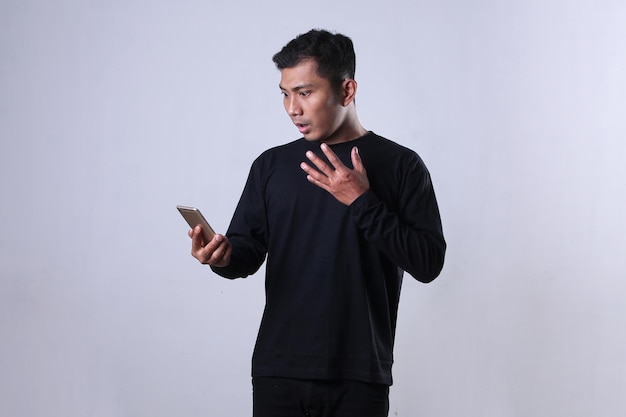 Zaskoczony wyraz twarzy Azjaty ubranego na czarno, patrzący na smartfona w dłoni