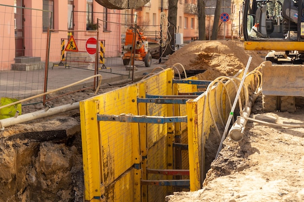 Zasypywanie koparką głębokiego wykopu podpartego skrzynią wykopową z podsypką rurową żwirem grochowym podczas montażu rury drenażowej