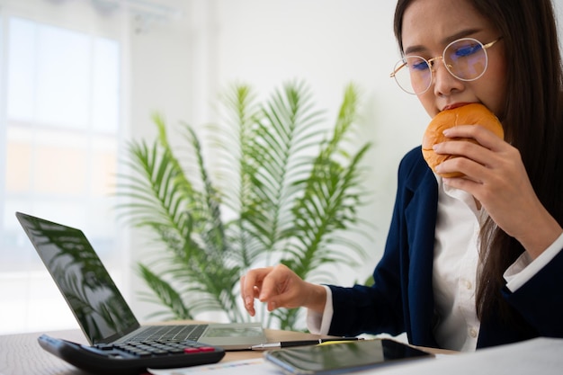 Zdjęcie zatrudniona i zmęczona bizneswoman jedząca chleb i mleko na obiad w biurze desk