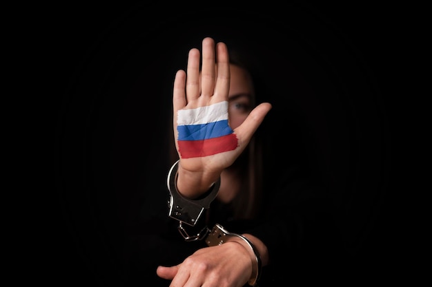 Zatrzymaj rosyjską dziewczynę w kajdankach gestem stop i rosyjską flagą narysowaną na jej dłoni