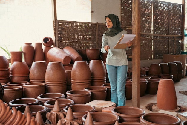 Zawoalowana bizneswoman licząca ceramikę trzymająca schowek na ceramicznym straganie