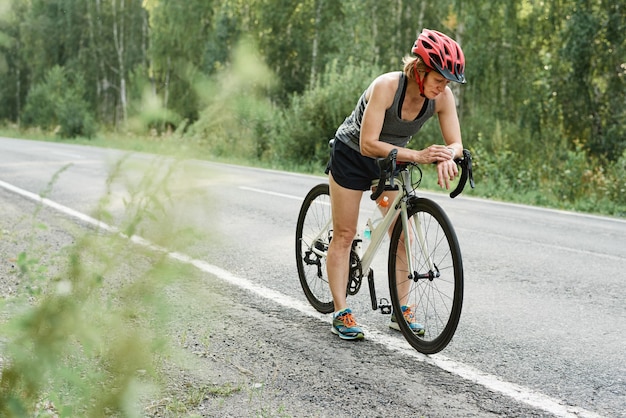 Zawodniczka W Kasku Sprawdza Swoją Bransoletkę Fitness Przed Jazdą Na Rowerze Po Wiejskiej Drodze