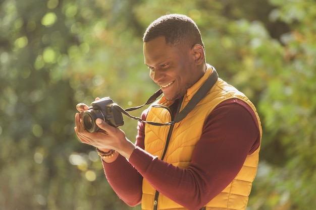 Zbliżenie african american facet fotograf robi zdjęcie aparatem fotograficznym na miasto zielony park rozrywki różnorodność i koncepcja hobby