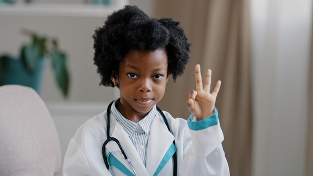 Zbliżenie Afroamerykanin mała dziewczynka stojąca w ubraniach medycznych grająca udając lekarza