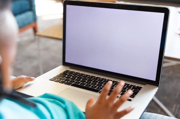 Zbliżenie afroamerykańskiego ucznia podstawowego używającego laptopa podczas siedzenia w szkole