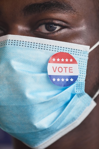Zbliżenie afrykańskiego wyborcy z pinezką z tekstem Głosuj na jego masce ochronnej