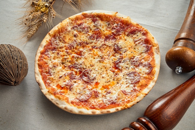 Zbliżenie apetycznej pikantnej pizzy z kiełbasą chorizo, serem i pieprzem na szarym lnianym obrusie w restauracji. Pizza w składzie. Kuchnia włoska. Jedzenie leżało płasko