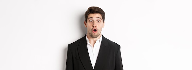 Zbliżenie atrakcyjnego mężczyzny w czarnym garniturze, wyglądającego na zaskoczonego i pod wrażeniem reklamy stojącej ov