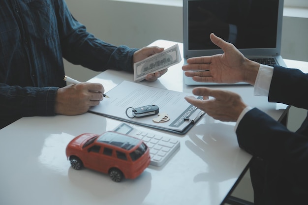 Zbliżenie azjatyckich mężczyzn sprzedawca samochodów lub kierownik sprzedaży oferuje sprzedaż samochodu oraz wyjaśnia i czyta warunki podpisania umowy samochodowej i ubezpieczenia