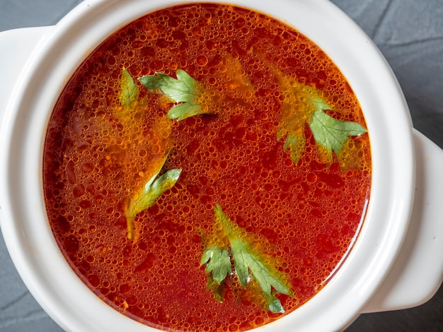 Zdjęcie zbliżenie barszcz zupy w białej ceramicznej misce zupy na szarym tle z teksturą tradycyjna zupa dla rosji i ukrainy zieloni unoszą się na wierzchu zupy widok z góry