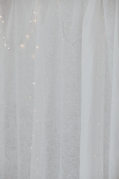 Zbliżenie białego tiulu kurtynowego i świecących świateł girlandy za estetycznym minimalistycznym tłem