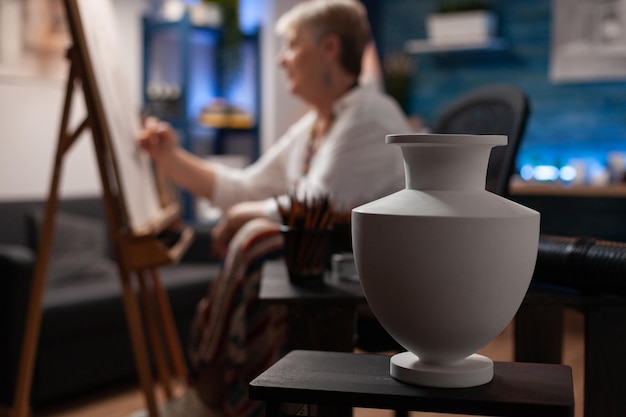 Zdjęcie zbliżenie biały wazon na drewnianym stole używany do inspiracji przez emerytowanego artystę rysującego ołówkiem na sztalugach w domu sztuki studio. selektywne skupienie się na martwym obiekcie używanym jako temat do szkicu w warsztacie.