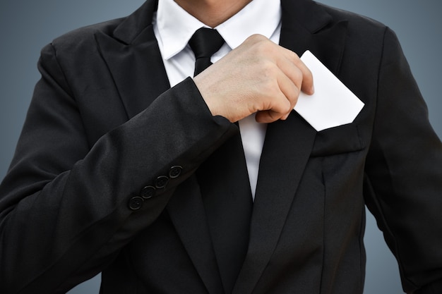 Zbliżenie biznesmen, który wyjmuje białą kartkę papieru z kieszeni w czarnym garniturze. Pomysł na biznesową kartę kredytową lub wizytówkę.