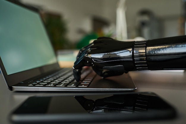 Zbliżenie biznesmena z protezą ramienia pracującego online, piszącego na laptopie przy stole