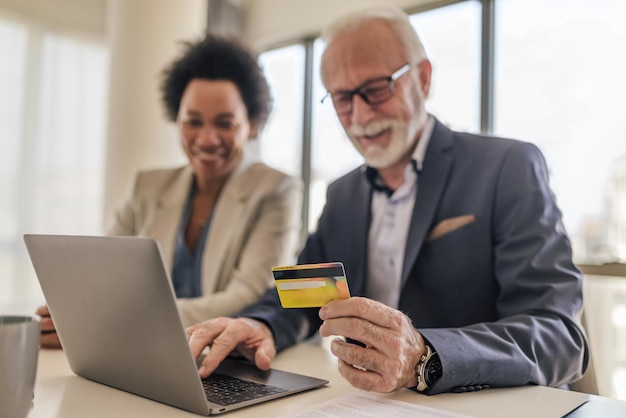 Zbliżenie biznesmena z współpracownikiem płacącym online z karty kredytowej na laptopie