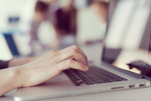 zbliżenie biznesowej kobiety ręcznie piszącej na laptopie na nowoczesnym komputerze biurowym startowym, zespół blured na spotkaniu, grupa ludzi w tle
