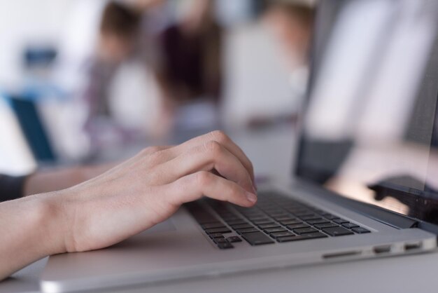 zbliżenie biznesowej kobiety ręcznie piszącej na laptopie na nowoczesnym komputerze biurowym startowym, zespół blured na spotkaniu, grupa ludzi w tle