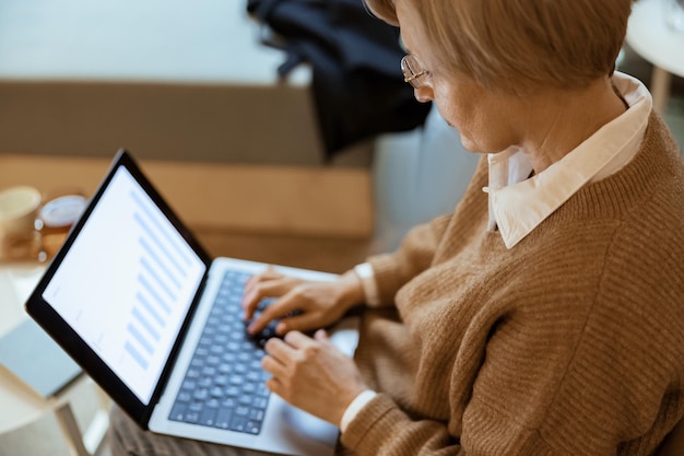 Zbliżenie bizneswoman w średnim wieku używającej laptopa pracuje z danymi statystycznymi w przytulnej kawiarni