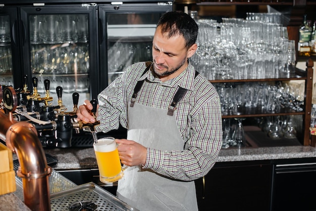 Zbliżenie: Brodaty Barman Napełniający Kubek Piwa Lager. Lada Barowa W Pubie.