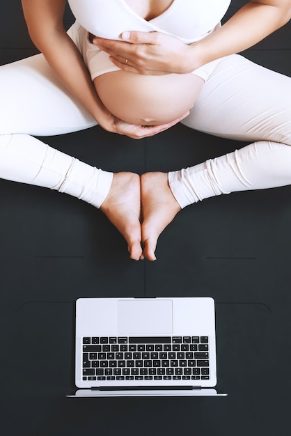 Zbliżenie Brzuch Kobiety W Ciąży ćwiczącej Jogę Online W Domu Z Laptopem