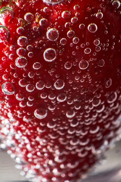 Zbliżenie całej truskawki pokrytej bąbelkami dwutlenku węgla na dnie szklanki z napojem bezalkoholowym