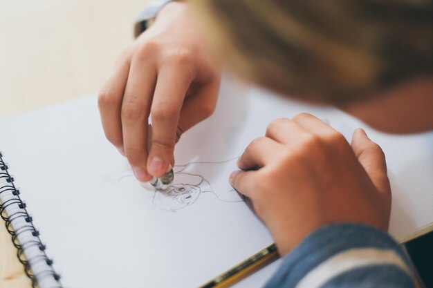 Zdjęcie zbliżenie chłopca rysującego na książce i wymazującego