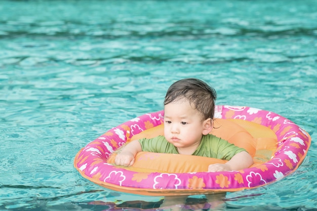 Zbliżenie chłopiec siedzi w łodzi dla dzieci w pływackiego basenu tle