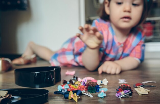 Zbliżenie Cute Dziewczynka Gra Z Kolekcji Spinki Do Włosów Leżąc W Drewnianej Podłodze W Domu. Selektywne Skupienie Się Na Spinkach Do Włosów.