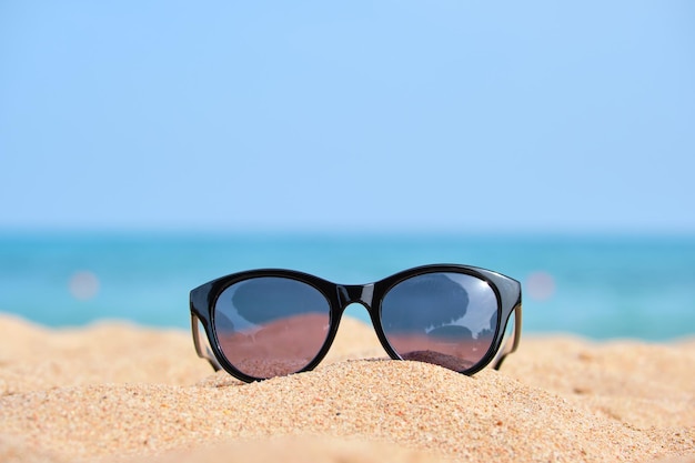 Zbliżenie czarne okulary ochronne na piaszczystej plaży w tropikalnym wybrzeżu w ciepły słoneczny dzień. Koncepcja wakacji letnich.
