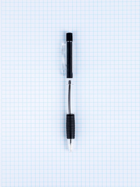 Zbliżenie czarnego długopisu leżącego na notatniku w kratkę gotowym do rozpoczęcia pracy