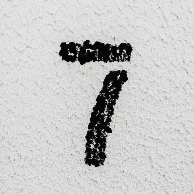 Zdjęcie zbliżenie czarnej malowanej liczby 7 na tle szarej teksturowanej ściany