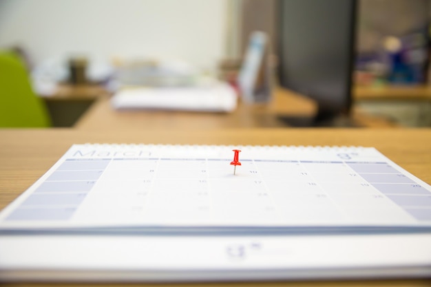 Zbliżenie czerwoną szpilkę na pustym kalendarzu biurkowym.