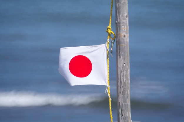Zdjęcie zbliżenie czerwonej flagi wiszącej na słupie na tle morza