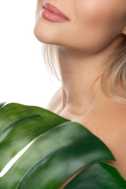 Zbliżenie części kobiecej twarzy z gładką skórą i zielonym tropikalnym liściem