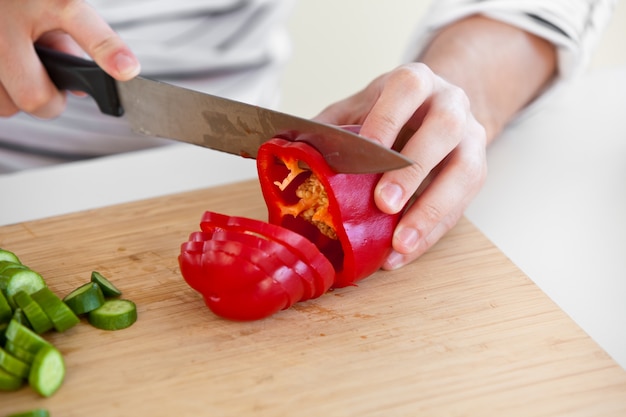 Zdjęcie zbliżenie człowieka cięcia czerwonego pieprzu stoi w kuchni