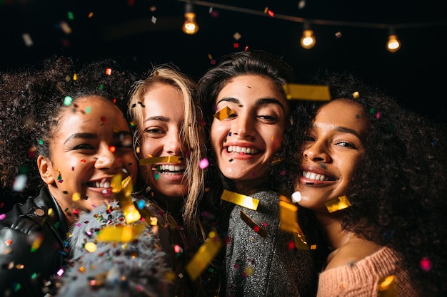 Zbliżenie czterech szczęśliwych kobiet pod konfetti robiących selfie w nocy