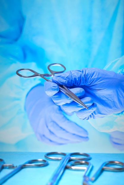 Zbliżenie dłoni chirurgów w pracy w sali operacyjnej stonowanych na niebiesko. Zespół medyczny wykonujący operację