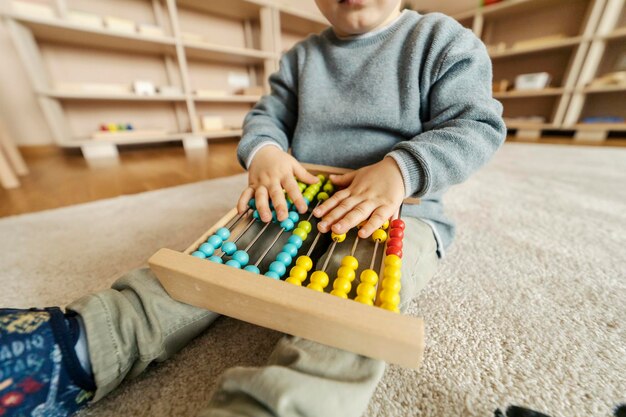 Zdjęcie zbliżenie dłoni chłopca dotykających kolorowego liczydła i bawiących się nim w przedszkolu montessori