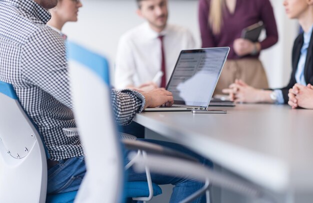 zbliżenie dłoni człowieka biznesu piszącego na laptopie w nowoczesnym biurze startowym, zespół blured na spotkaniu, grupa ludzi w tle