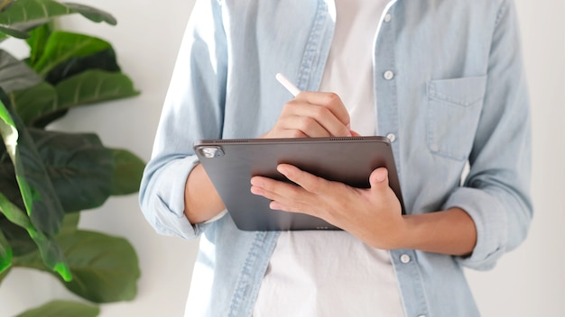 Zbliżenie dłoni człowieka pisania na cyfrowym tablecie podczas pracy w domu, studium online, telekomunikacja