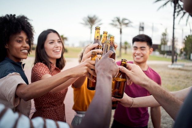Zbliżenie dłoni grupy młodych ludzi różnych ras wznoszących toast szczęśliwie na okrzyki słońca
