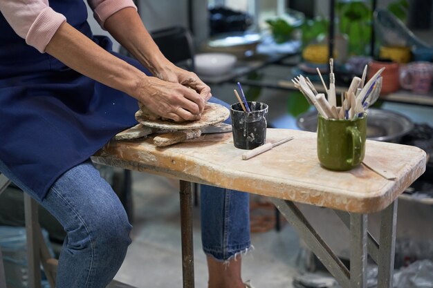 Zbliżenie dłoni kobiety kształtującej, tworzącej ręcznie robioną glinianą miskę ceramiczną w pracowni garncarskiej