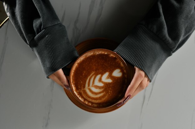 Zbliżenie dłoni kobiety trzymającej filiżankę amerykańskiej kawy z grubą pianką, gorącym napojem cappuccino,